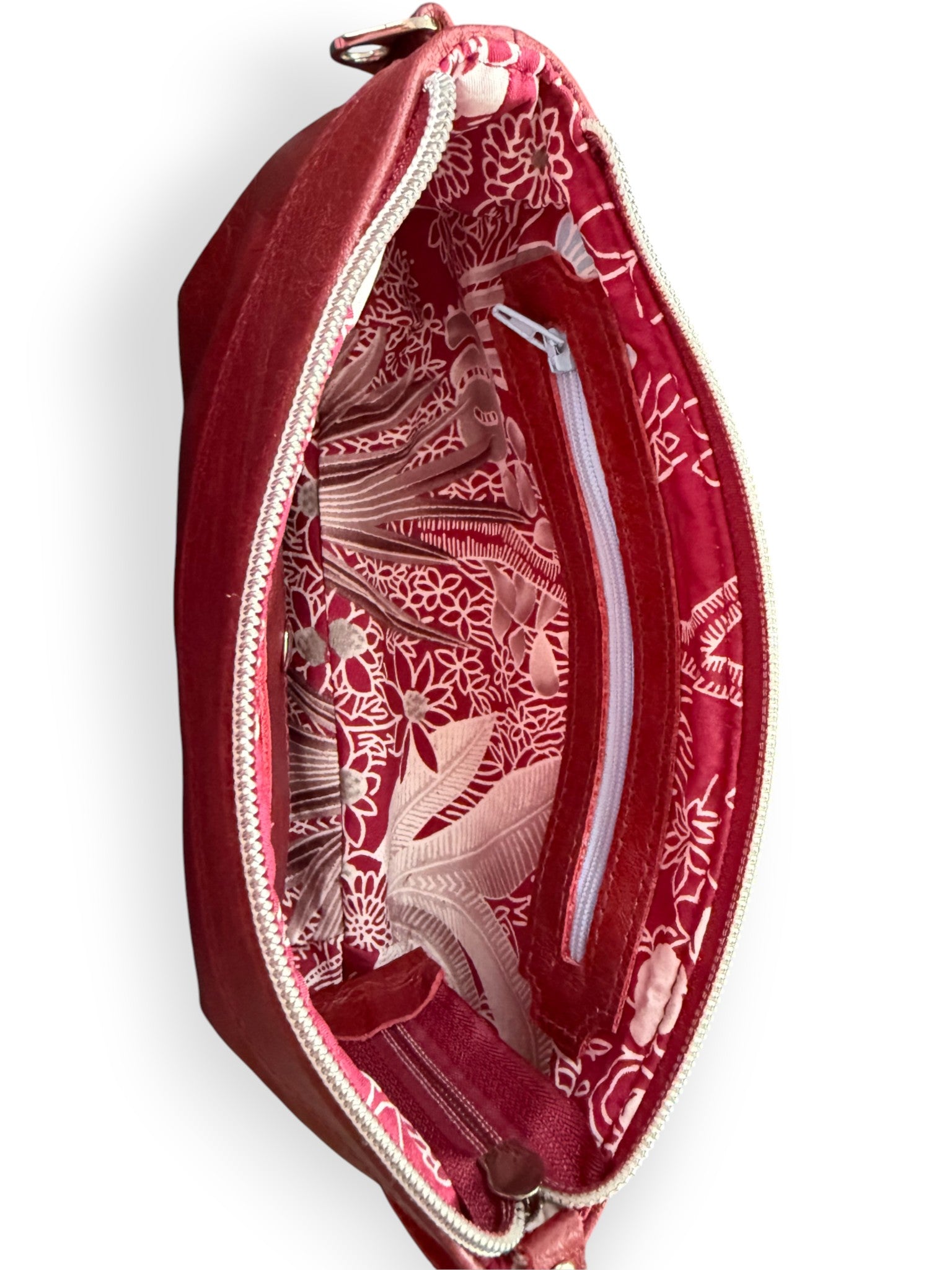 View of the dark red leather Ella clutch bag from above. The image shows the interior, with it's botanical patterned lining and the interior zipper pocket.