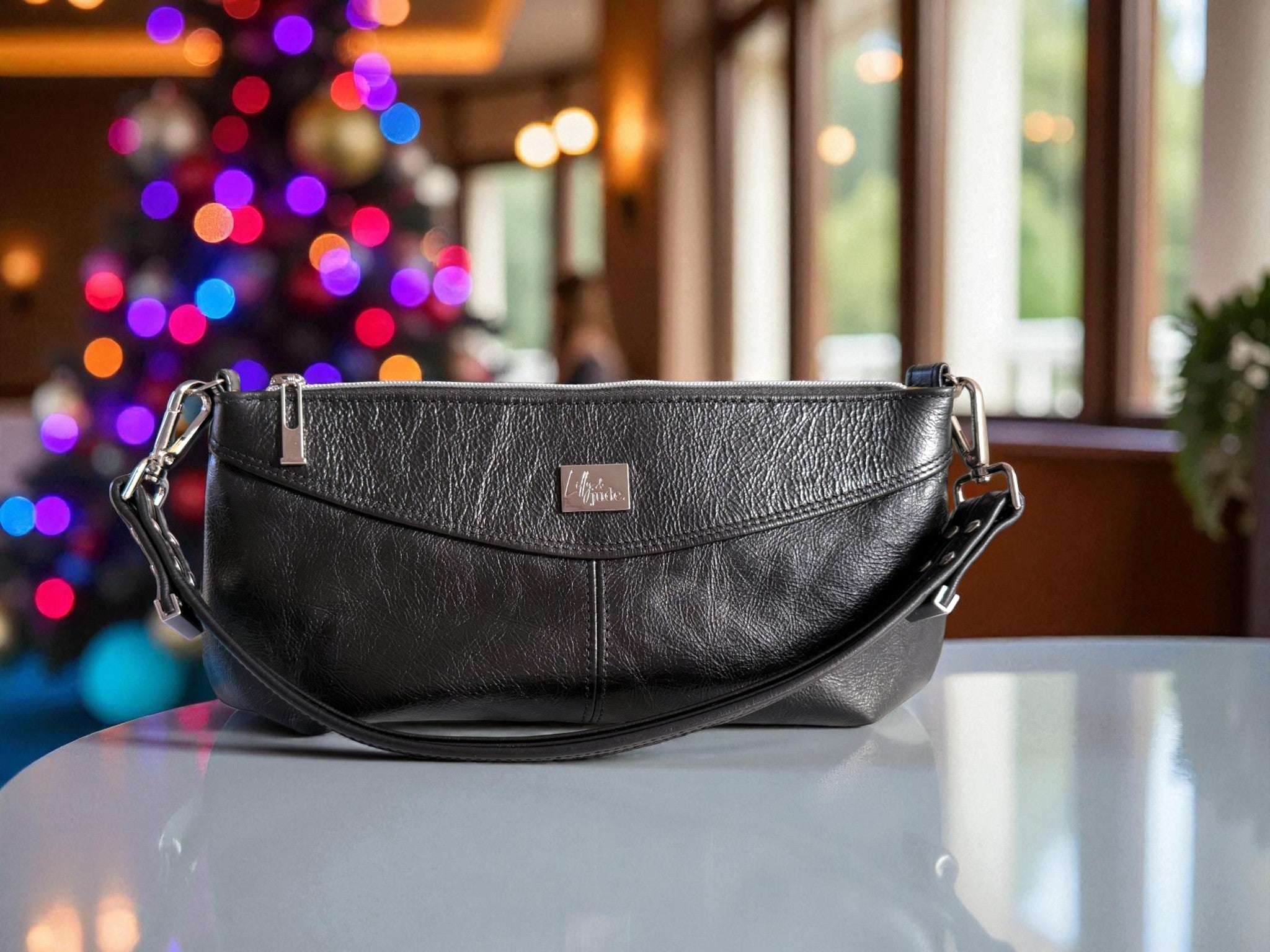 Black, rescued leather Elland handbag on a table with a blurred Christmas tree in the background