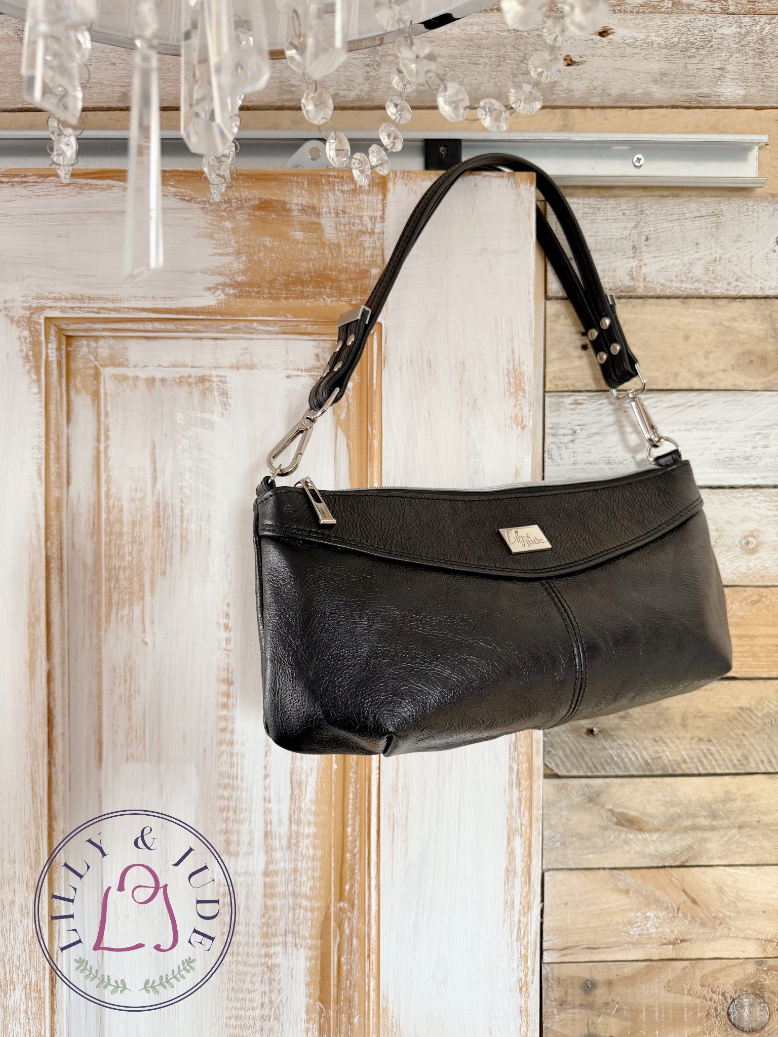Black leather Elland, baguette style handbag hanging on a wooden wall with a chandelier above