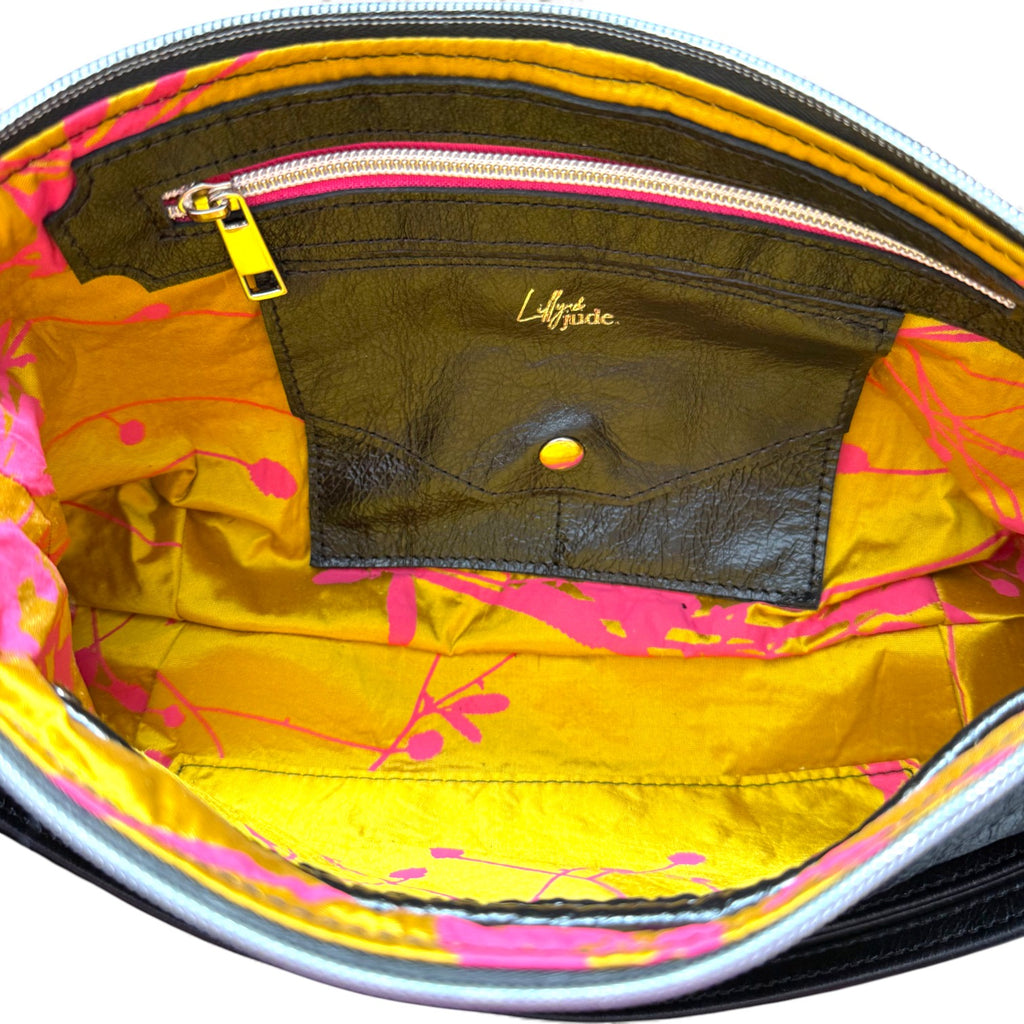 Close-up of a yellow gold and fuchsia pink bag patterned silk interior with a visible brand logo.The image shows the detail of the lining, including the leather trimmed hot pink zipper pocket and the integrated leather purse