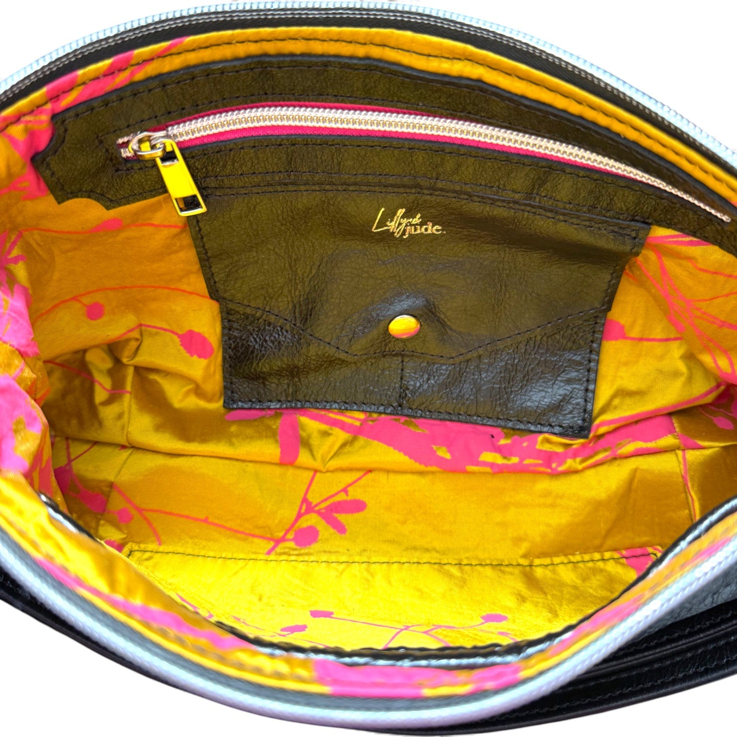 Close-up of a yellow gold and fuchsia pink bag patterned silk interior with a visible brand logo.The image shows the detail of the lining, including the leather trimmed hot pink zipper pocket and the integrated leather purse