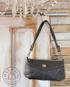 Charcoal grey leather handbag hanging on a wooden door with a chandelier in the background