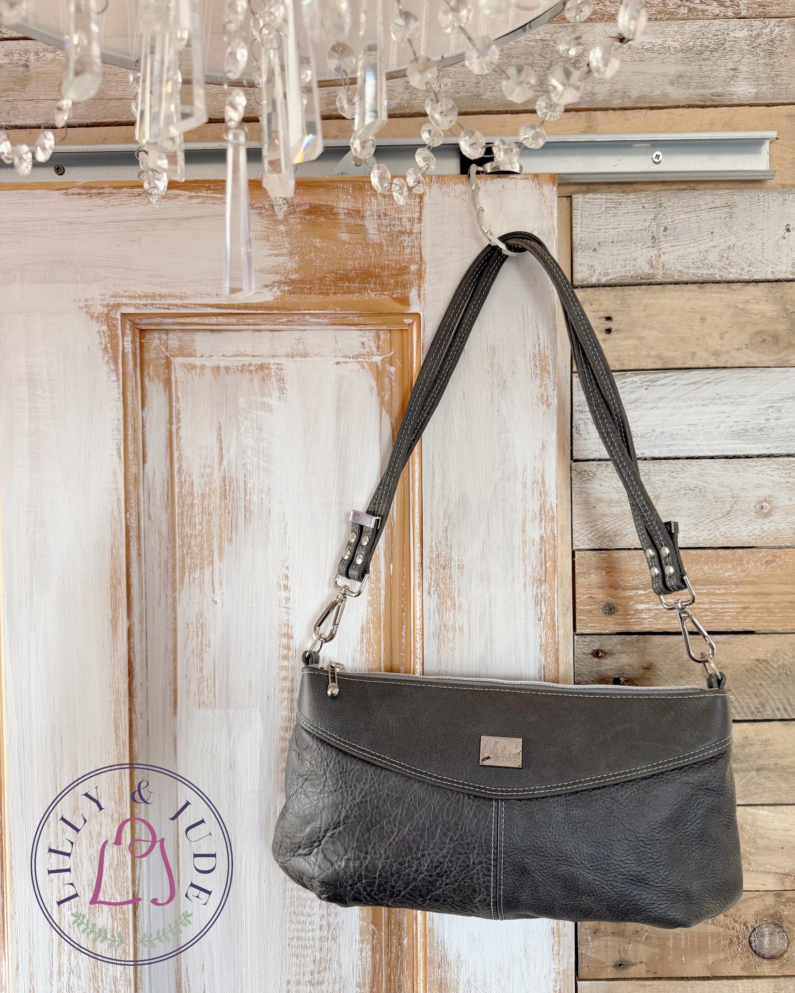 Charcoal grey leather handbag hanging on a wooden door with a chandelier in the background