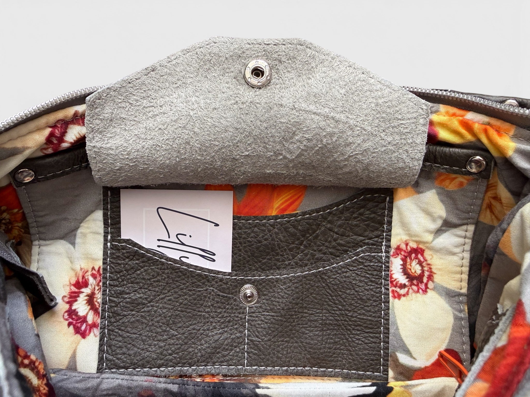 Close-up of a floral-patterned bag interior with a grey leather integrated purse and visible brand label.