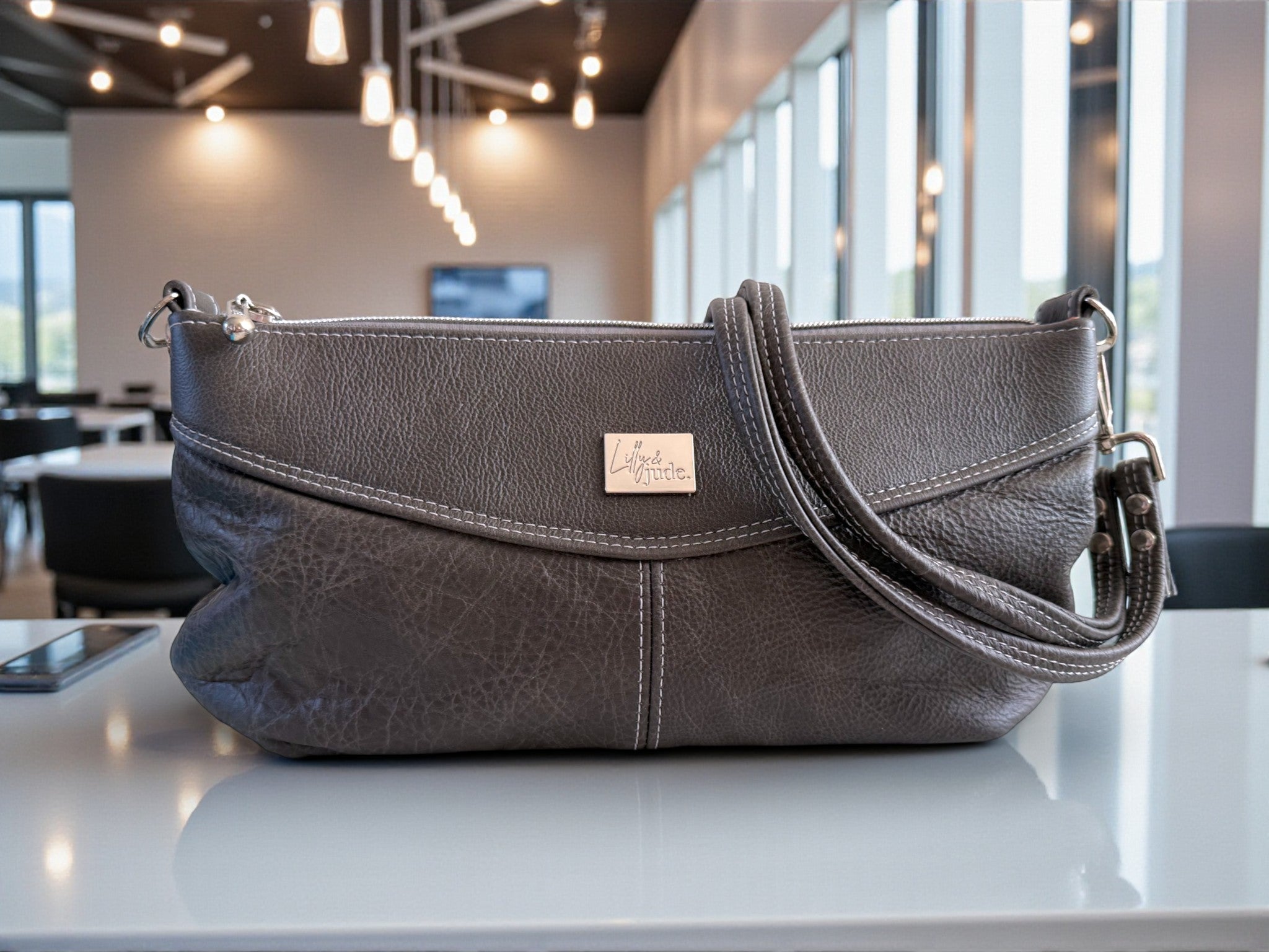 Charcoal grey handbag with a visible brand logo on a white surface in an indoor setting.