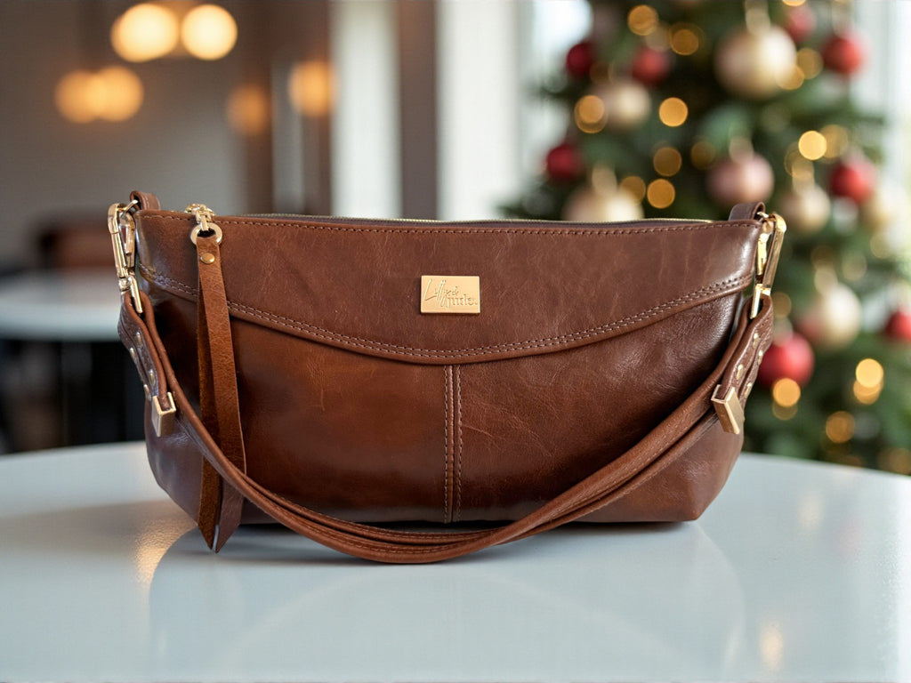 Chestnut brown coloured east/west style handbag, made from rescued leather sat on a table with a beautifully decorated Christmas tree in the background