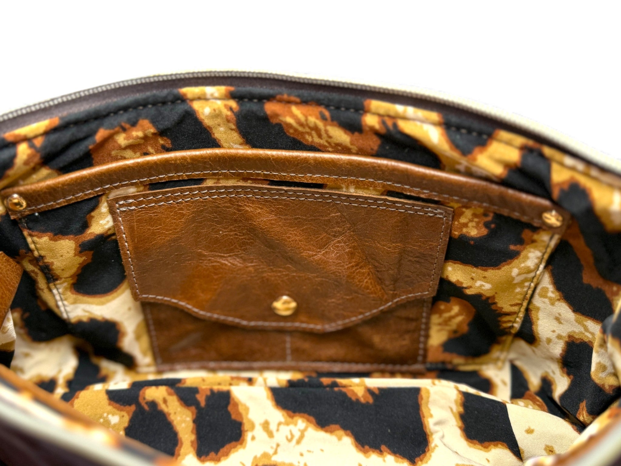 Interior view of a brown leather handbag with a leopard print lining and integrated leather purse