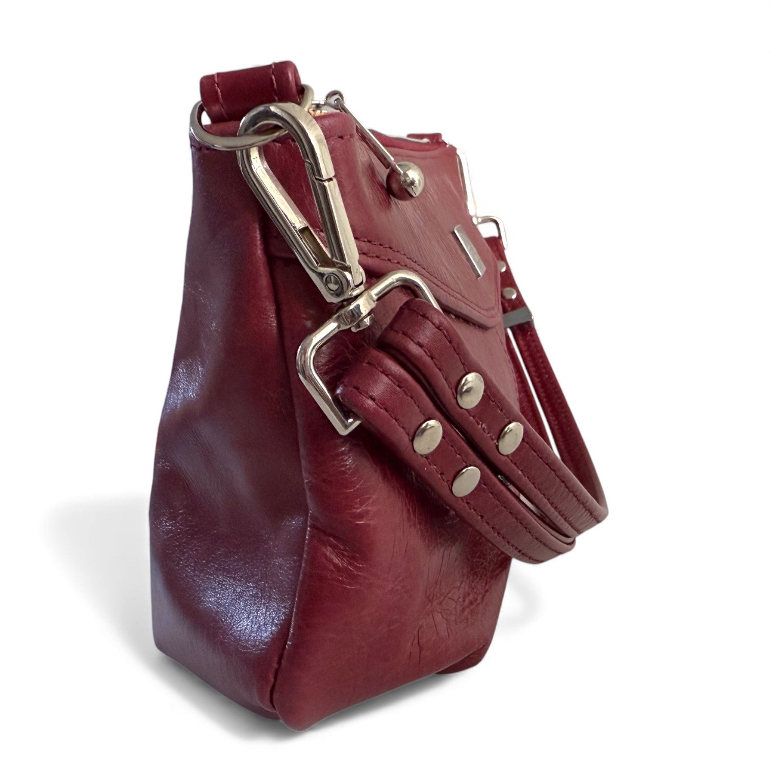 Red leather handbag with silver hardware on a white background. Closeup view of the side of the Elland bag, showing the detailing of the bag connector and strap