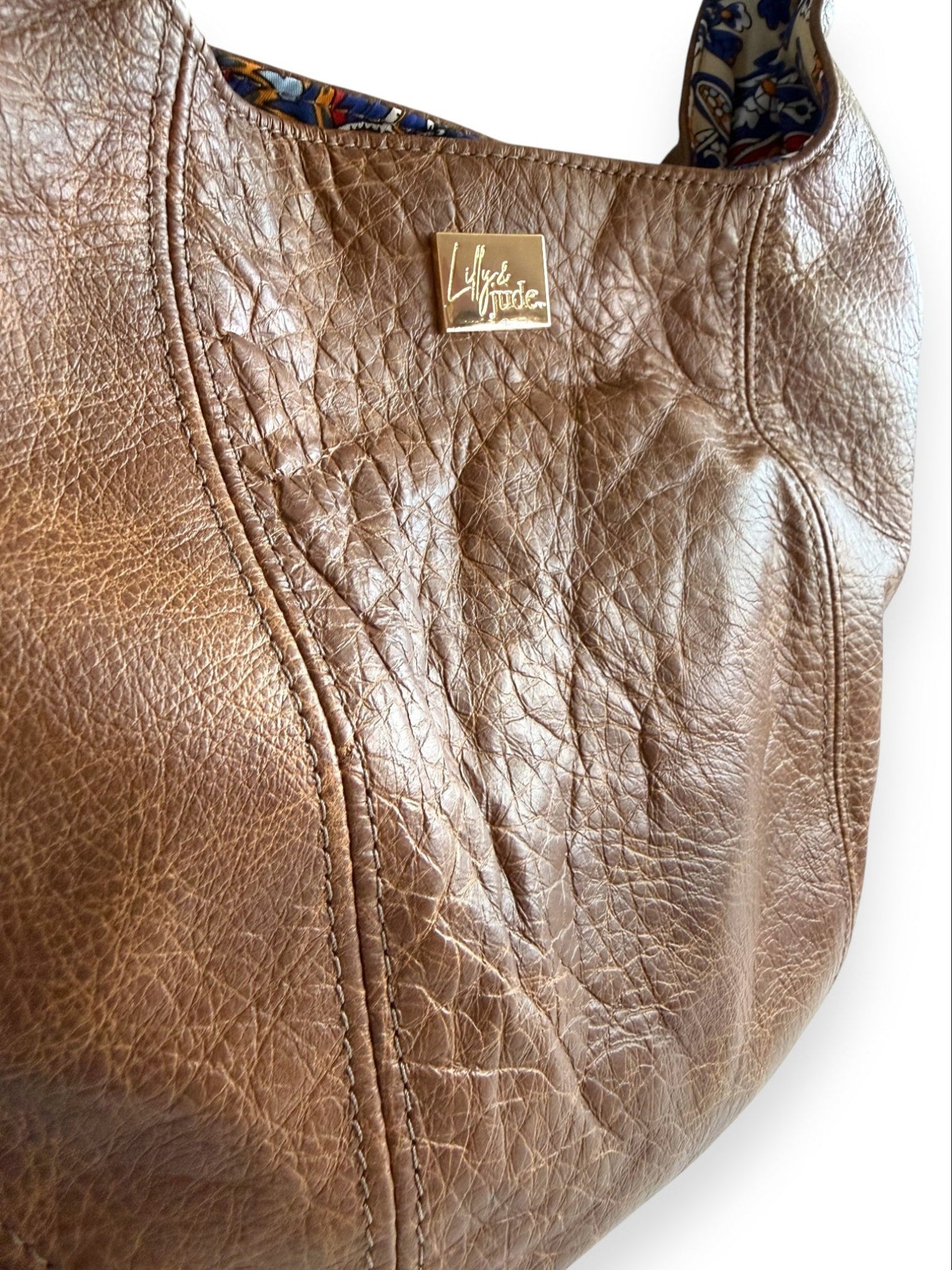 Closeup view of the Estrella in distressed, brown leather handbag, highlighting the softness and texture of the leather, with a visible Lilly & Jude brand logo tag on a white background