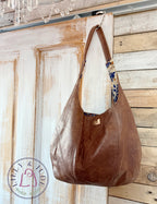 Brown, rescued leather handbag hanging on a wooden door with a rustic background