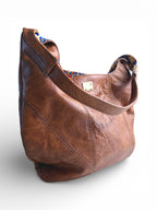 Front quarter view of the Estralla, a brown, disressed style leather handbag with a patterned interior on a white background