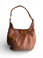 Brown, distressed, genuine leather handbag with paisley patterned interior on a white background