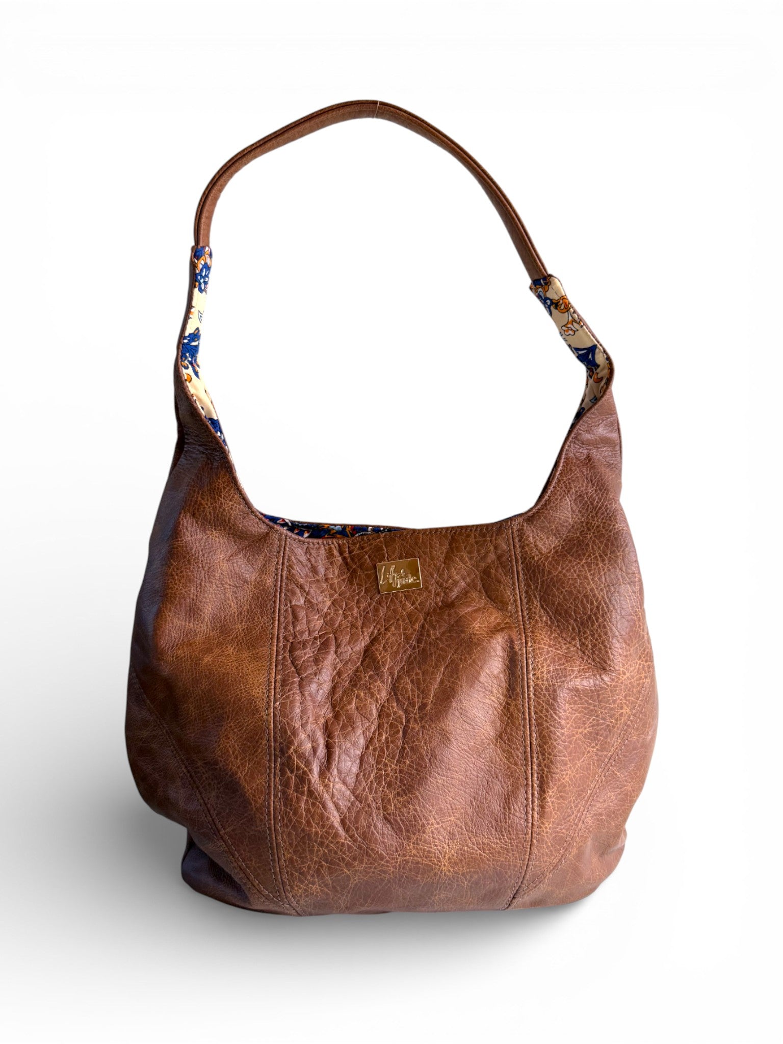 Brown, distressed, genuine leather handbag with paisley patterned interior on a white background