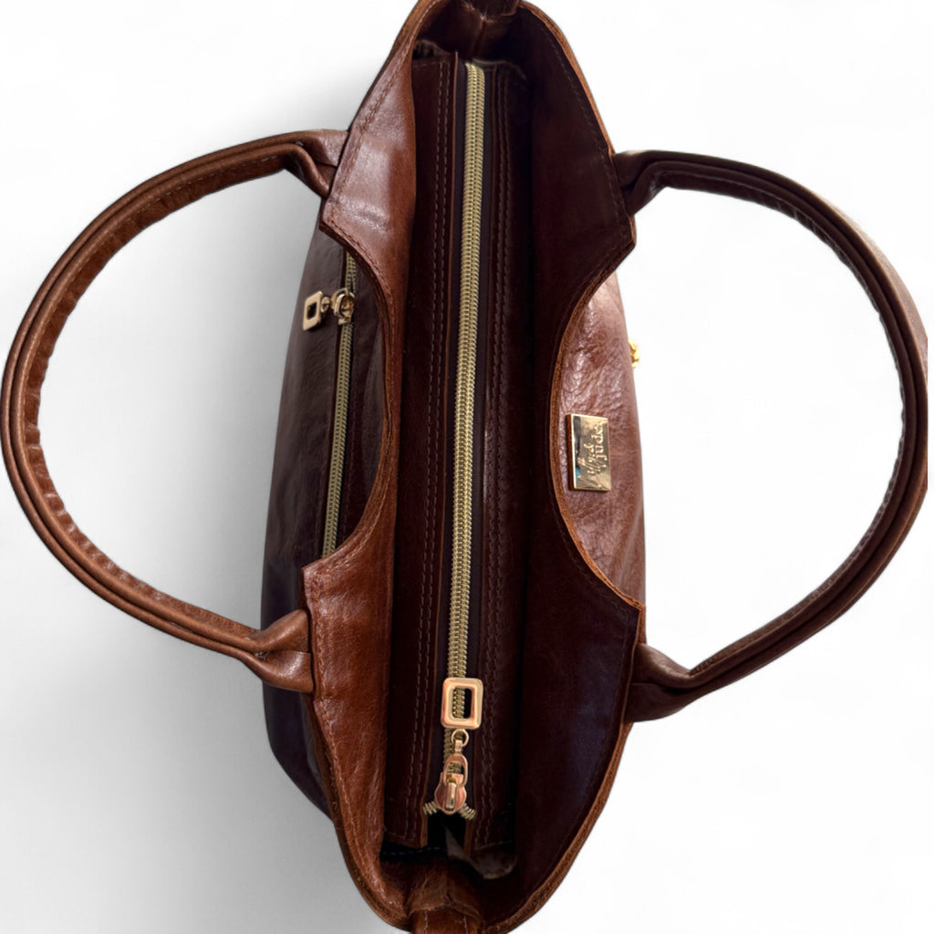 Birds Eye view of the Flossy Handbag. A chestnut brown leather bag with gold zipper on a white background. The image highlights the detailing of the zipper opening, and leather handles