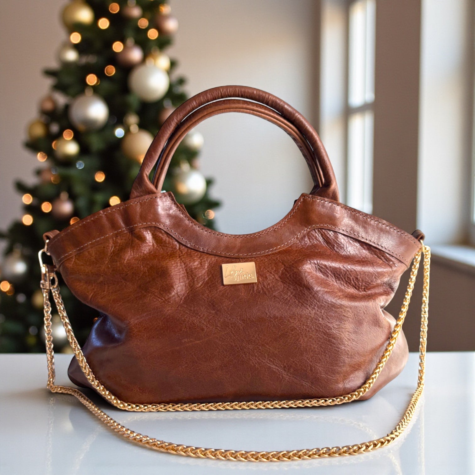 Brown Flossy handbag, handmade from rescued leather, with gold hardware, against a festive background, showing that it is perfect as a Christmas gift