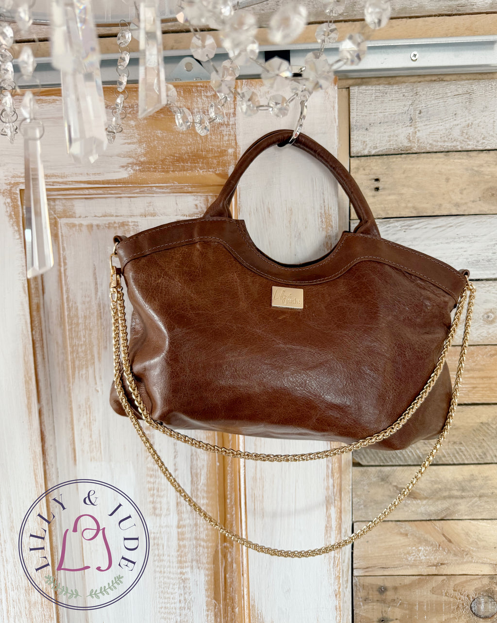 Brown leather handbag with gold chain strap hanging against a rustic wooden wall.