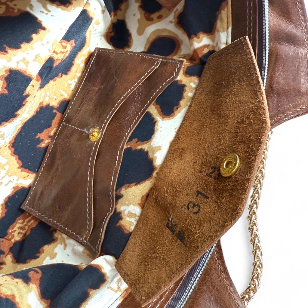 Close-up of a brown leather handbag with a chain detail and the leopard print lining. The image highlights the open integrated leather purse, with the flap open and the markings of the leather maker stamped on the suede side