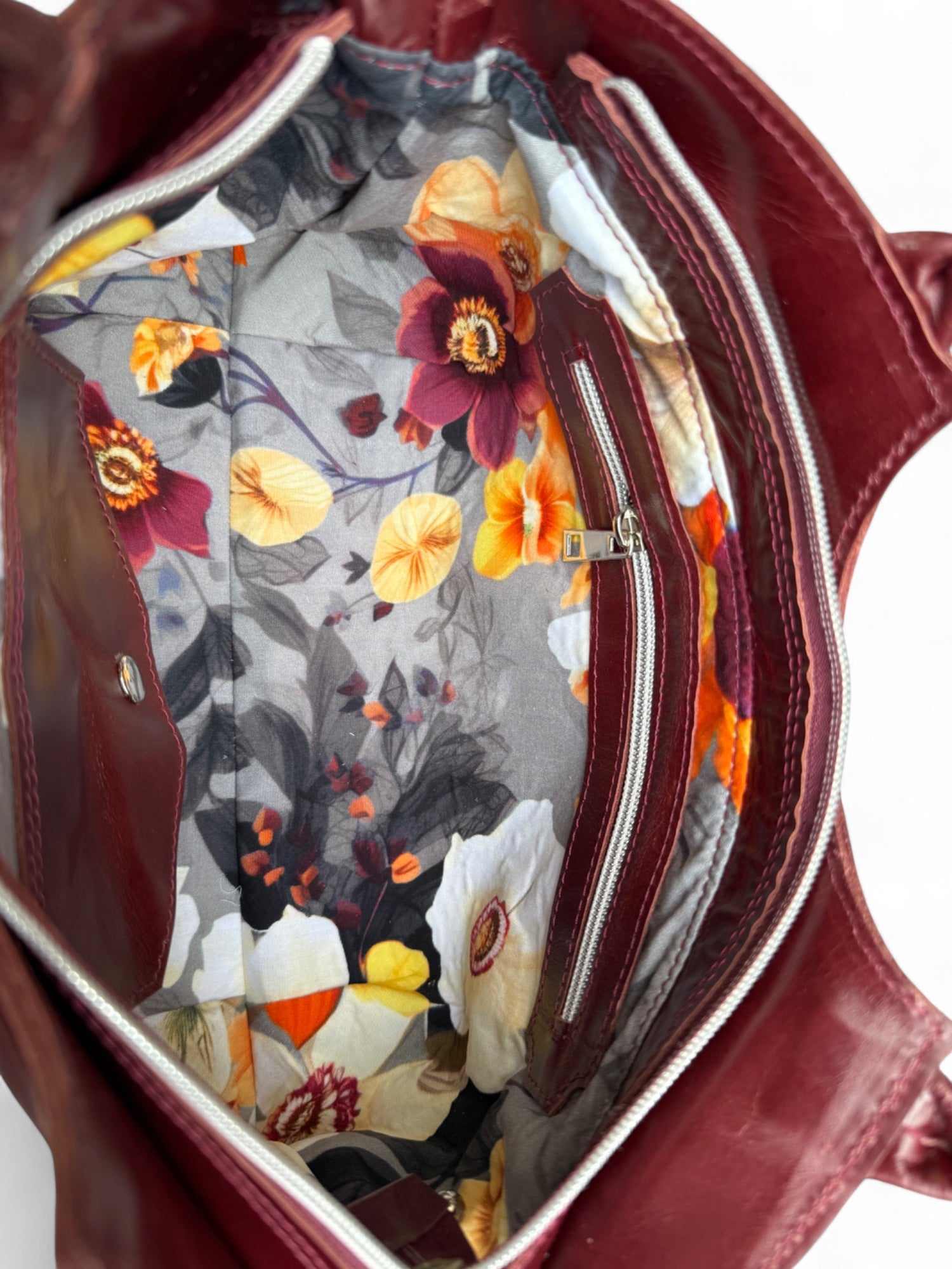 Floral pattern lining, inside a deep plum coloured handbag, showing the interior zipper pocket. The Flossy is handmade from rescued leather in the UK