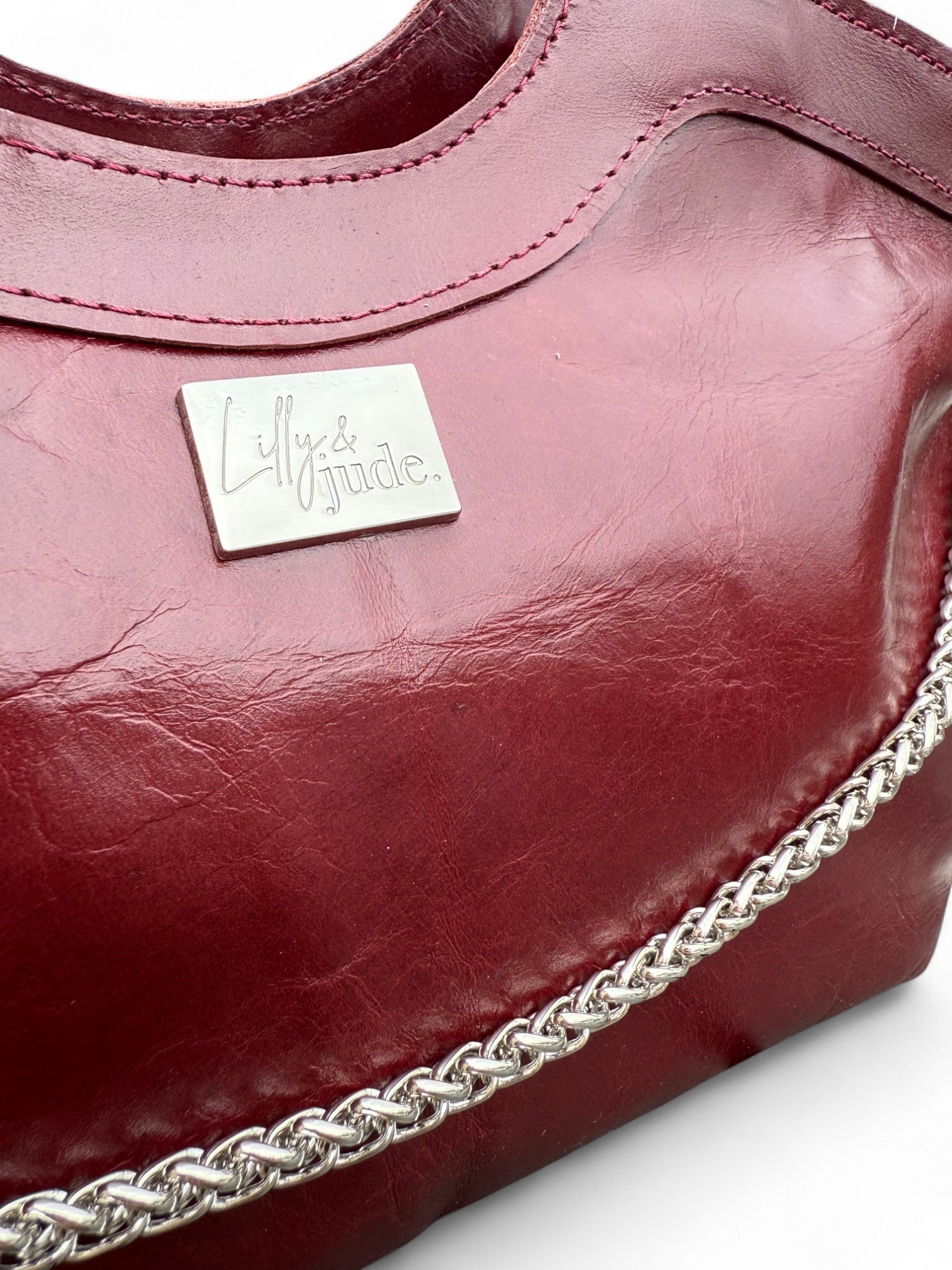 Close-up of a maroon handbag with the Lilly & Jude  brand logo on a white background