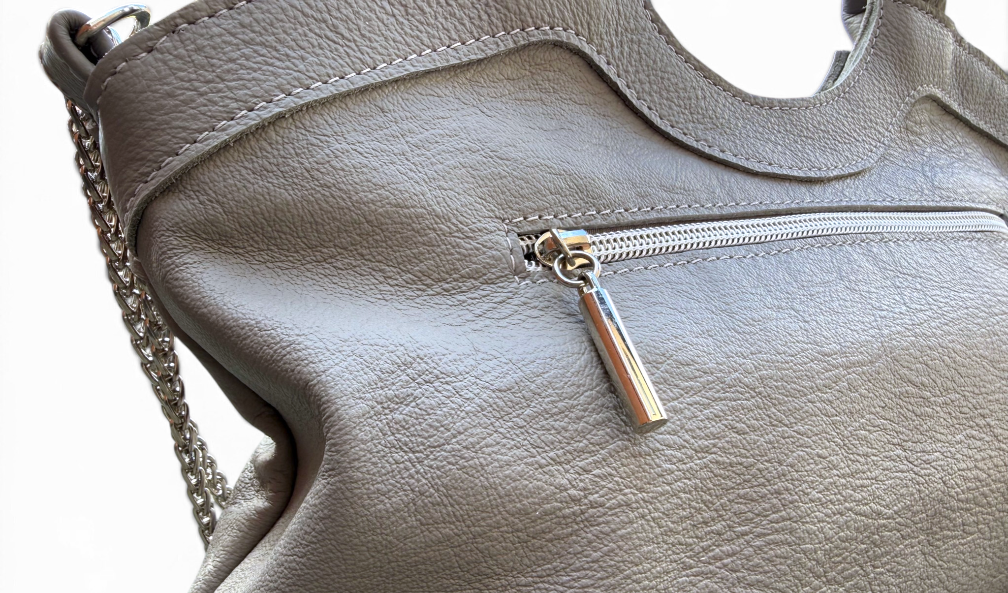Close-up of a taupe gray pebbled leather handbag with a silver zipper pocket and a silver chain strap on a white background.