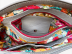 Close-up of the interior of a handbag showing a colourful floral-patterned lining, a light grey leather interior pocket, and a red zipper.