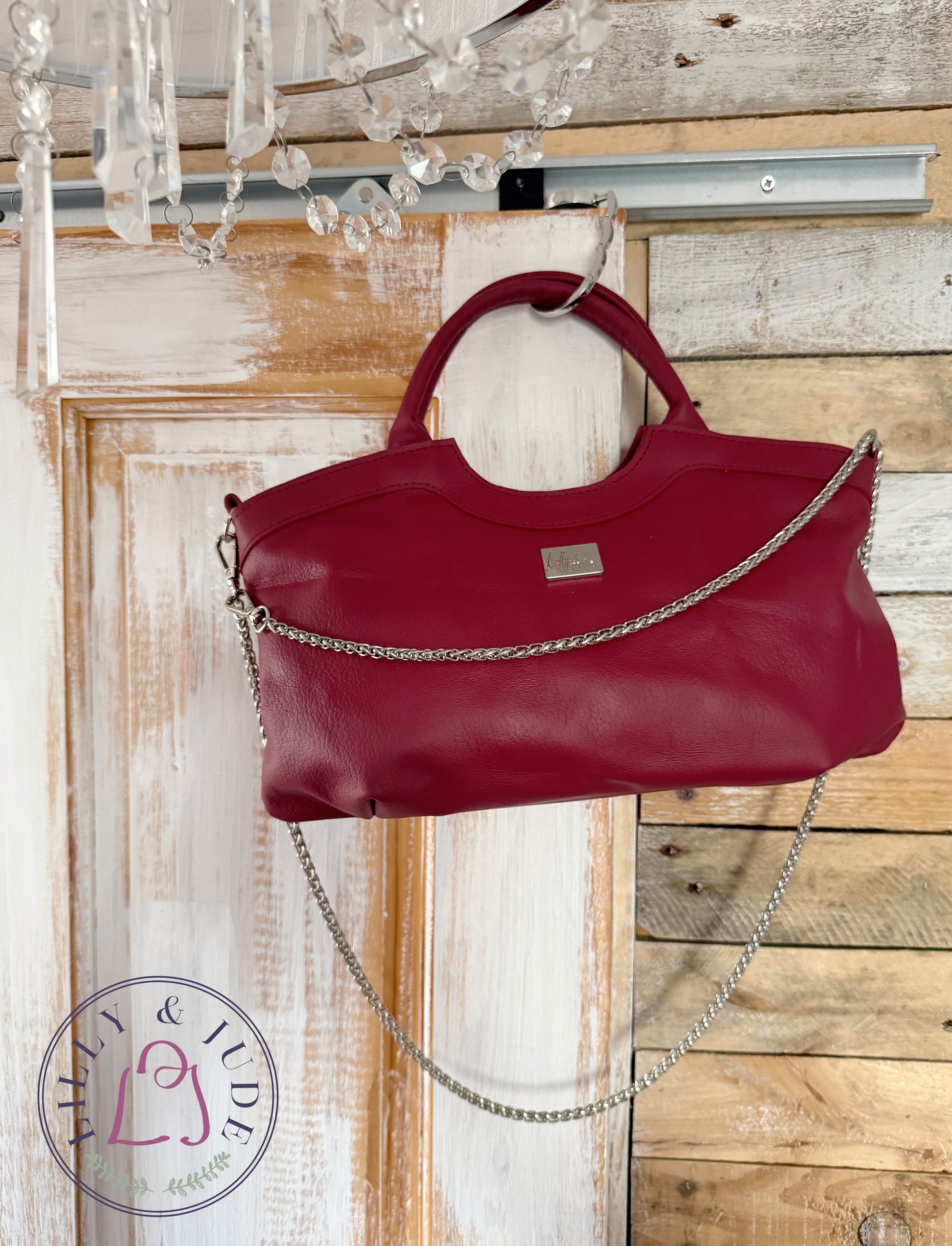 Red leather handbag with a silver chain detail hanging on a wooden door