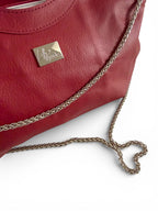 Closeup shot of the red, genuine leather handbag with a silver chain strap, arranged in a heart shape, on a white background