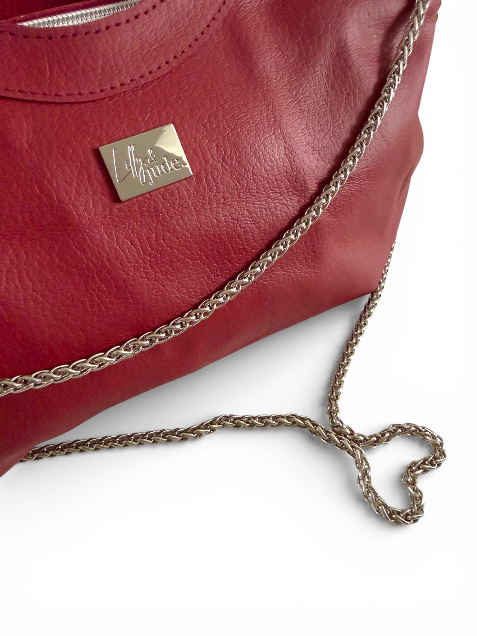 Closeup shot of the red, genuine leather handbag with a silver chain strap, arranged in a heart shape, on a white background
