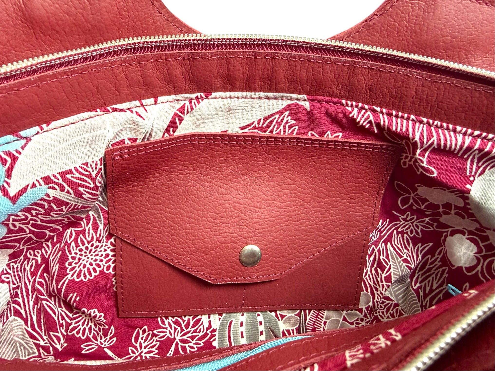 Close-up of  the interior of the Flossy a red leather handbag. The shot highlights the raspberry red and pale blue lining fabric and the Lilly & Jude signature integrated purse / wallet