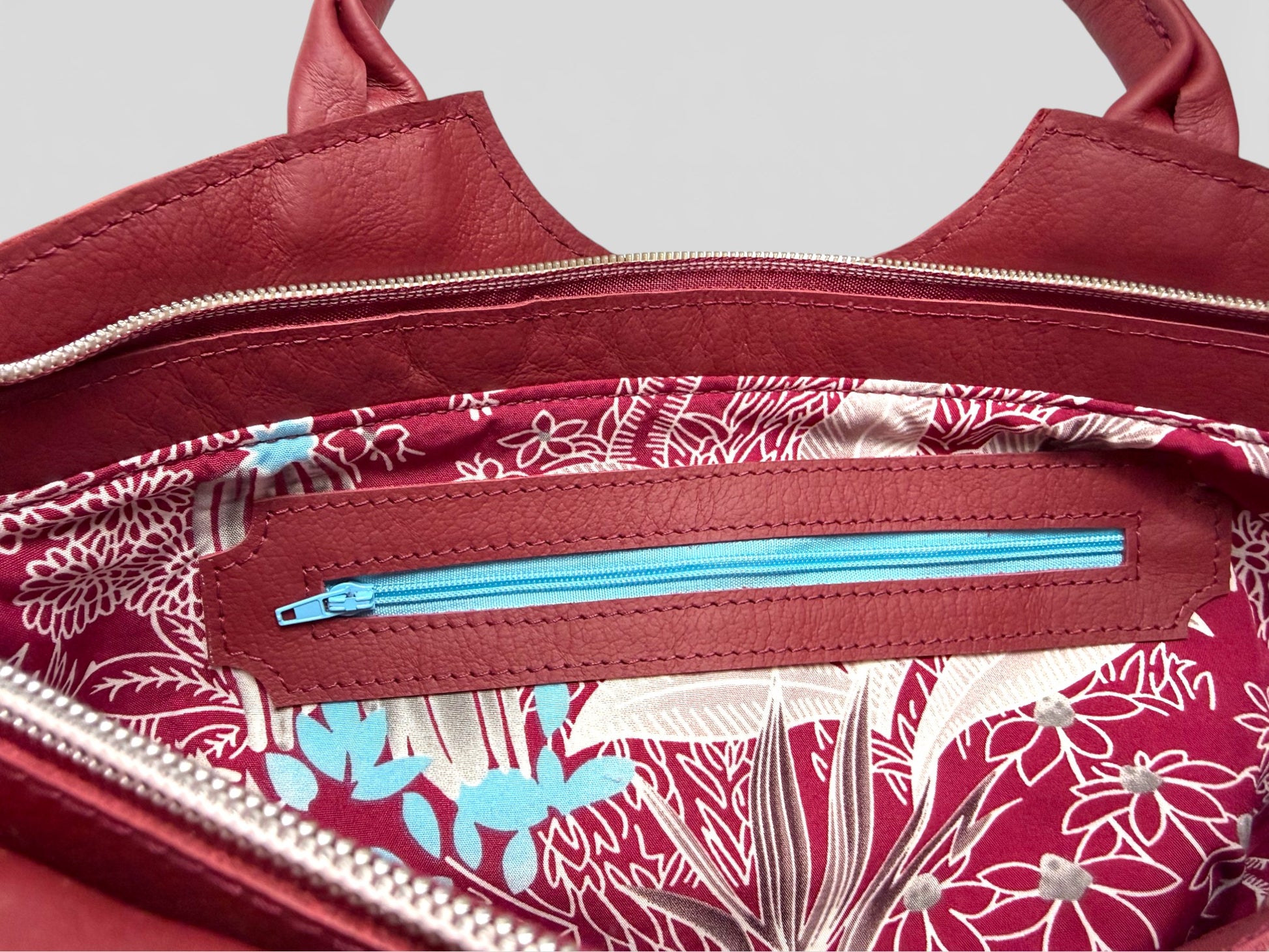 Interior view of the red Flossy bag, showing the floral-patterned lining, in raspberry red and pale blue highlights with a matching blue zipper on the interior zipper pocket