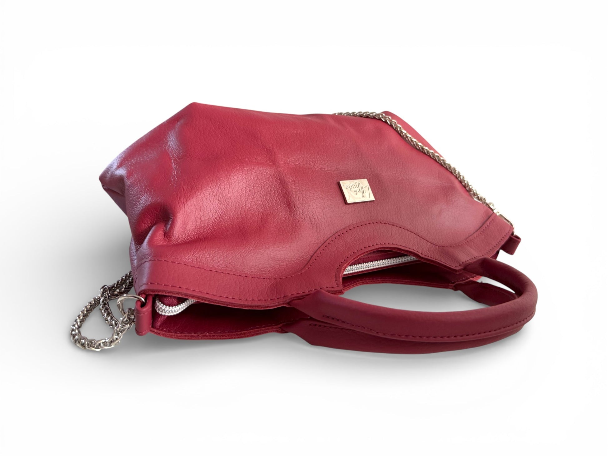 Red leather handbag, lying down with a silver chain on a white background