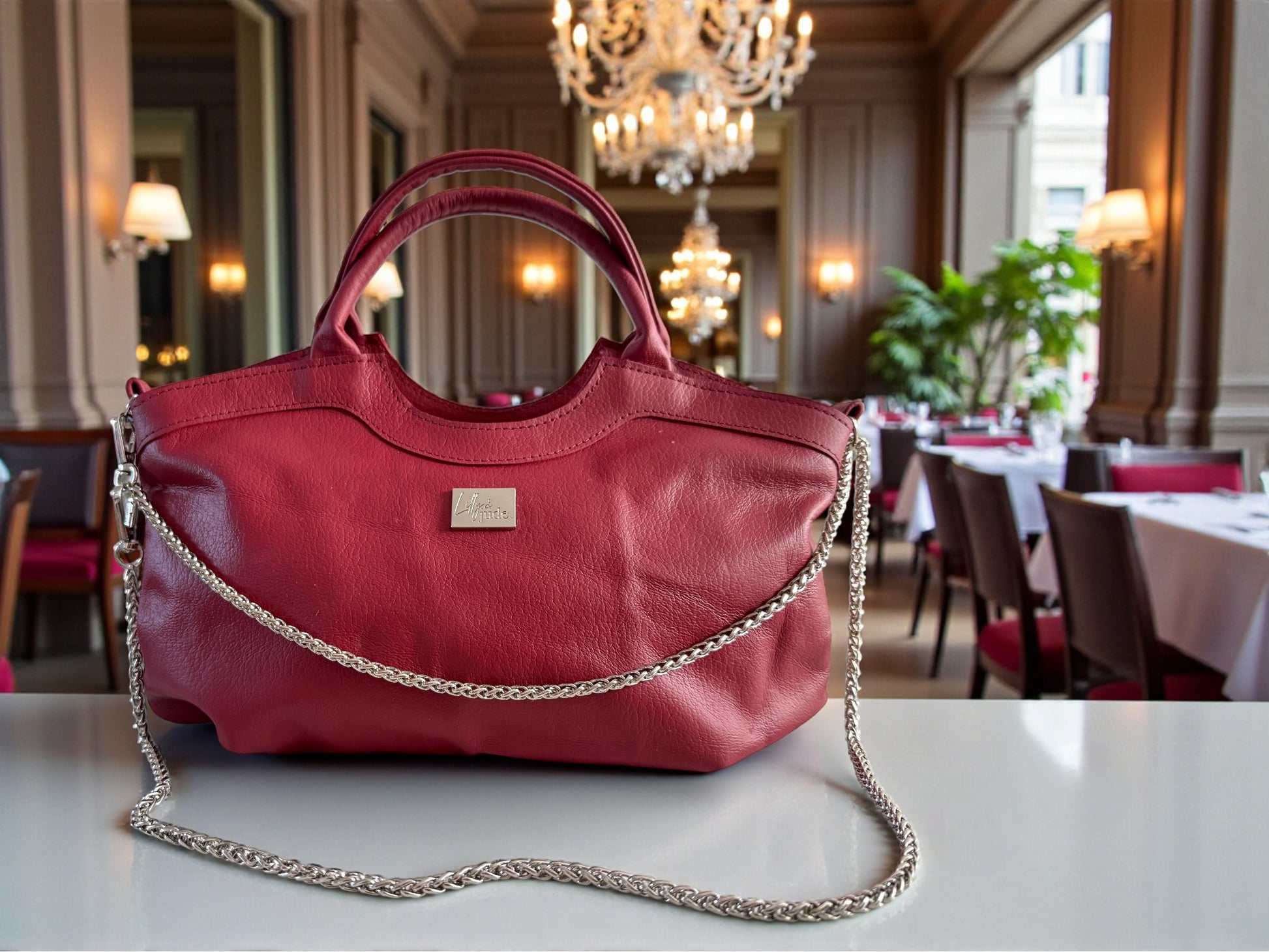 Lifestyle shot of a Red, Flossy handbag with a chain detail on a table in an elegant dining room.