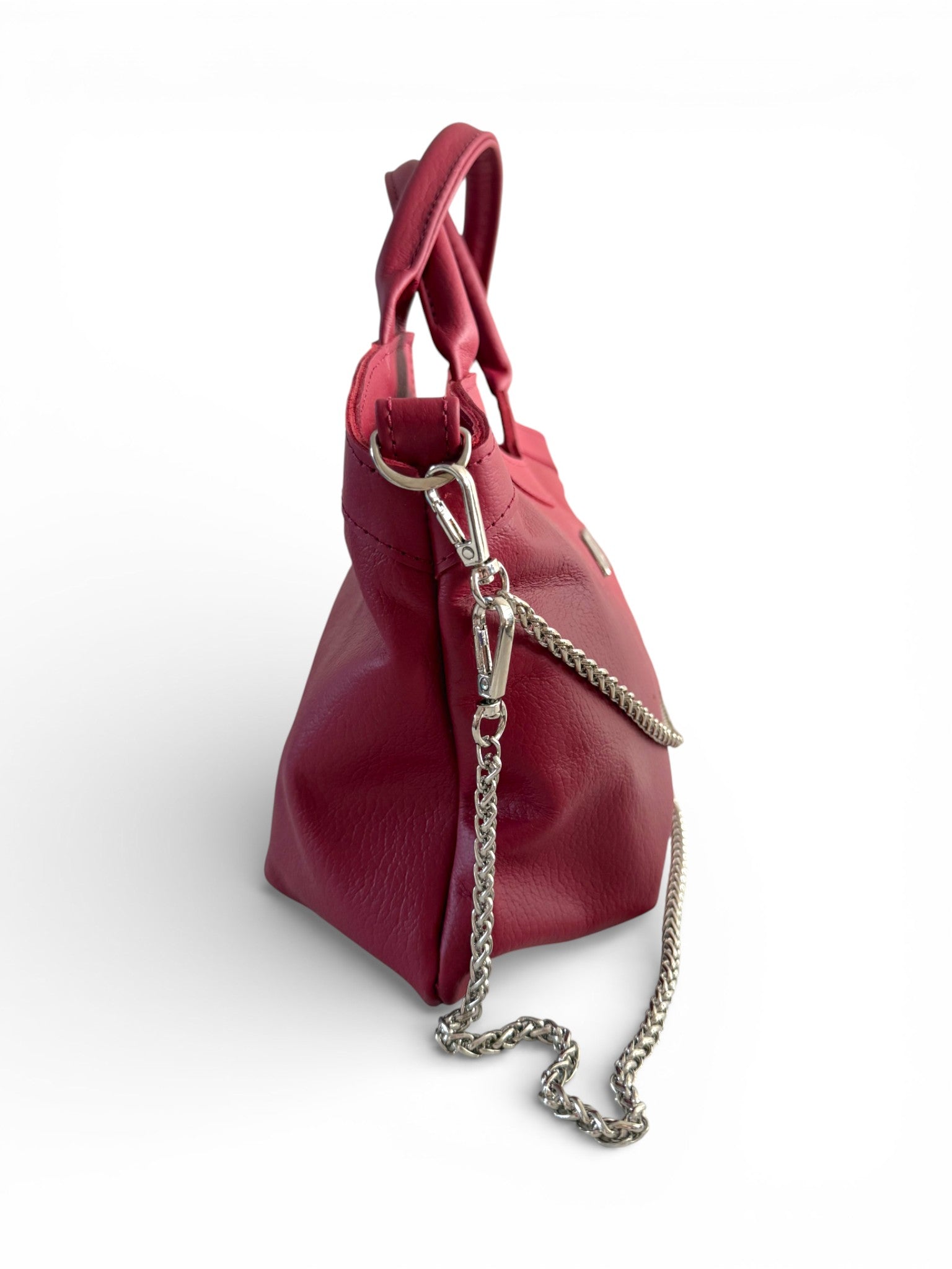 Side-on view of the red genuine leather handbag with a chain detail, sitting on a white background. The image highlights the detail of the strap connectors