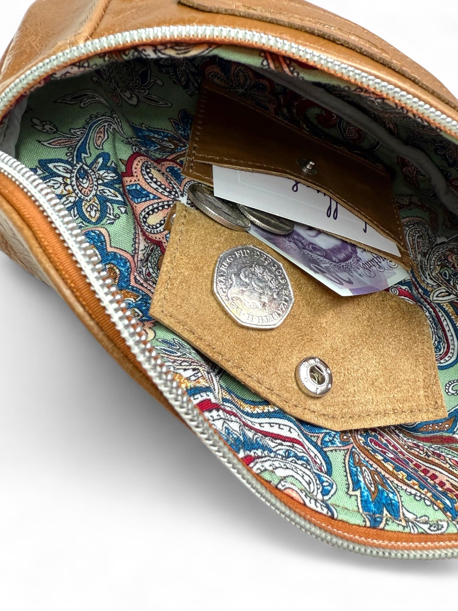 Open brown leather pouch with paisley pattern interior, showing coins and cash.