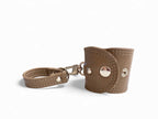 Taupe leather accessory cuff with metal clasps on a white background