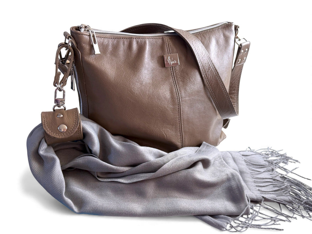 Taupe leather handbag with a grey scarf and accessory cuff on a white background