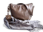 Taupe leather handbag with a grey scarf and accessory cuff on a white background