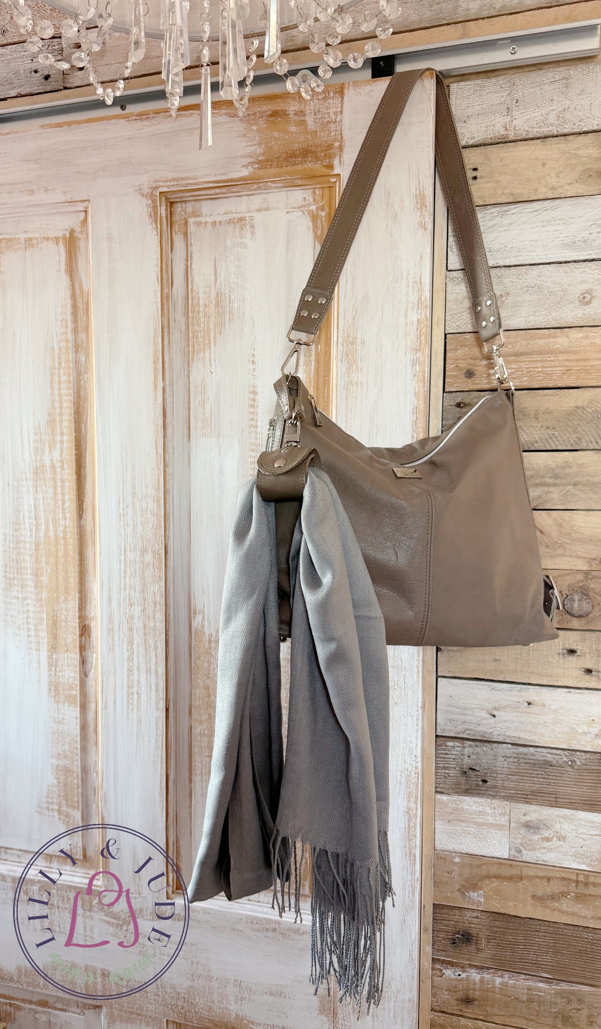 Grey taupe handbag with a grey scarf draped through a matching accessory cuff, against a wooden wall.