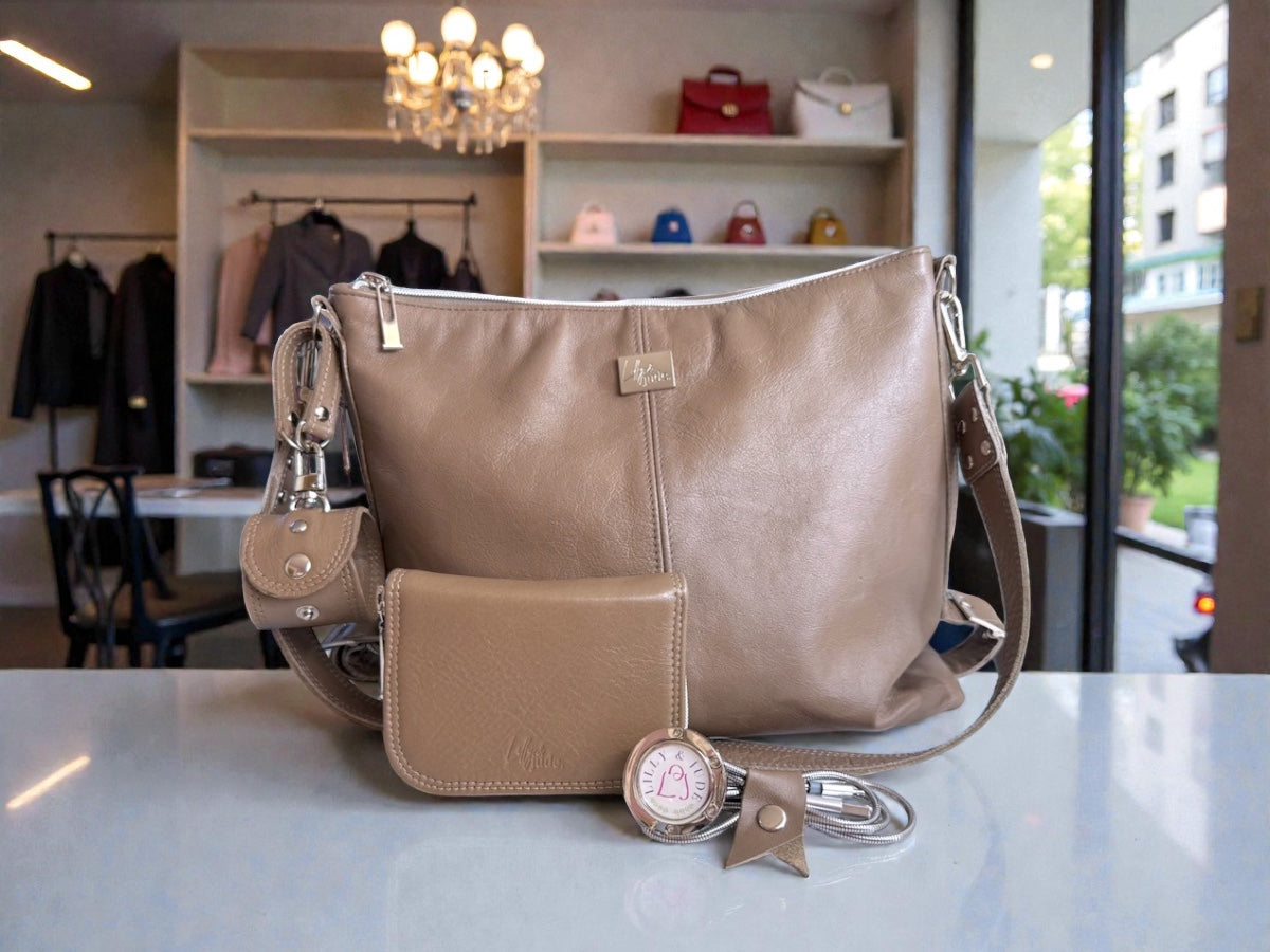 Beige taupe leather handbag with matching wallet/purse, accessory holder, bag hook and cable keeper, on a white table in a fashion boutique