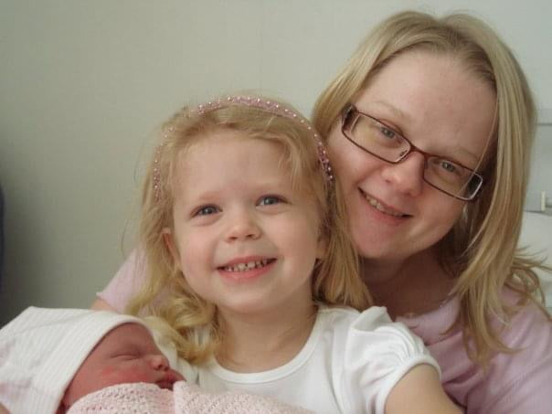 Woman with glasses holding a young girl and a baby, all smiling.
