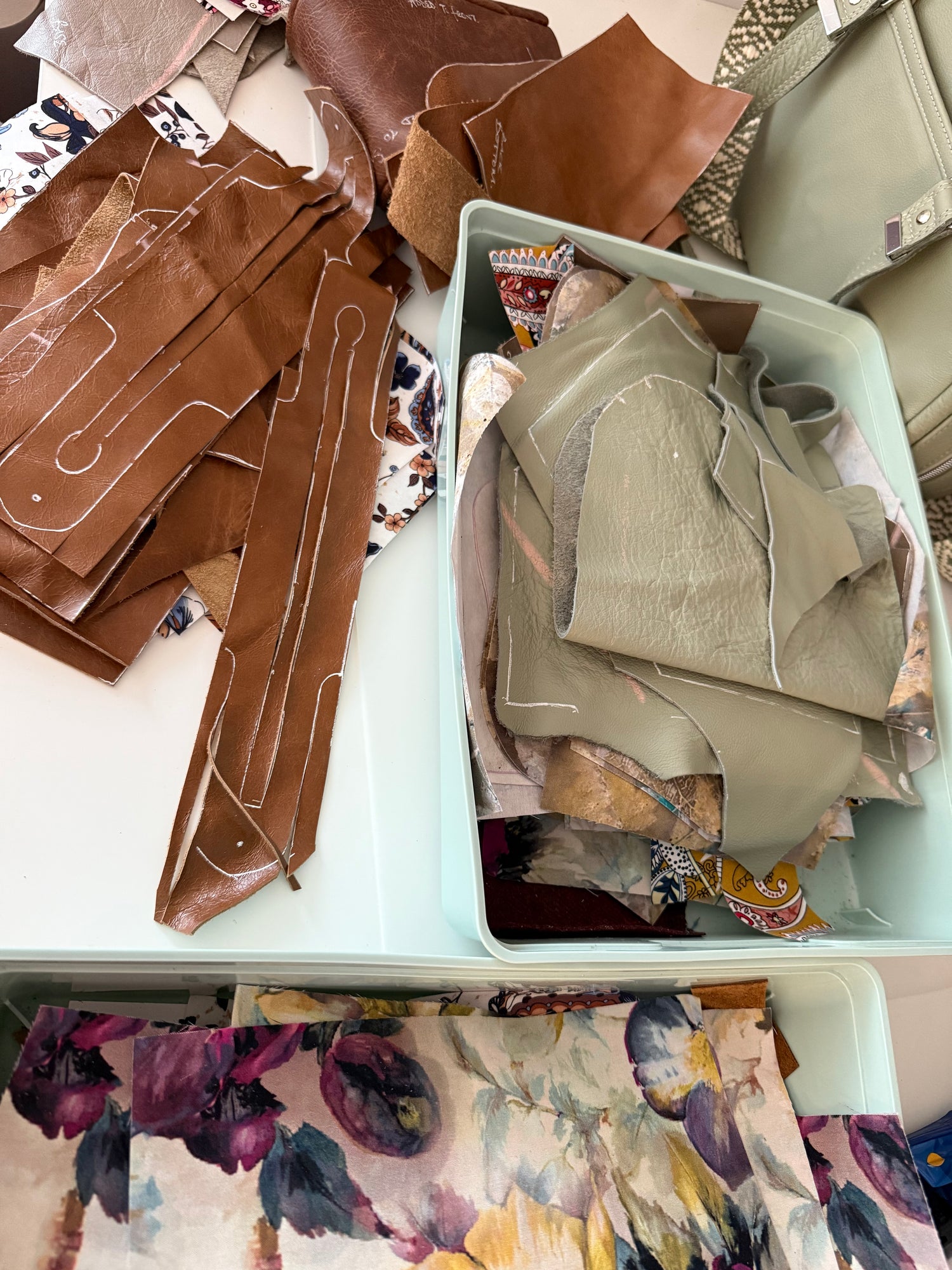 Leather pattern pieces in a container with various coloured fabrics on a table