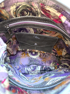 Close-up of the interior of a handbag showing a purple and orange floral patterned lining, a dark grey leather interior pocket with a silver zipper, and a leather brand label reading 'Lilly & Jude'.