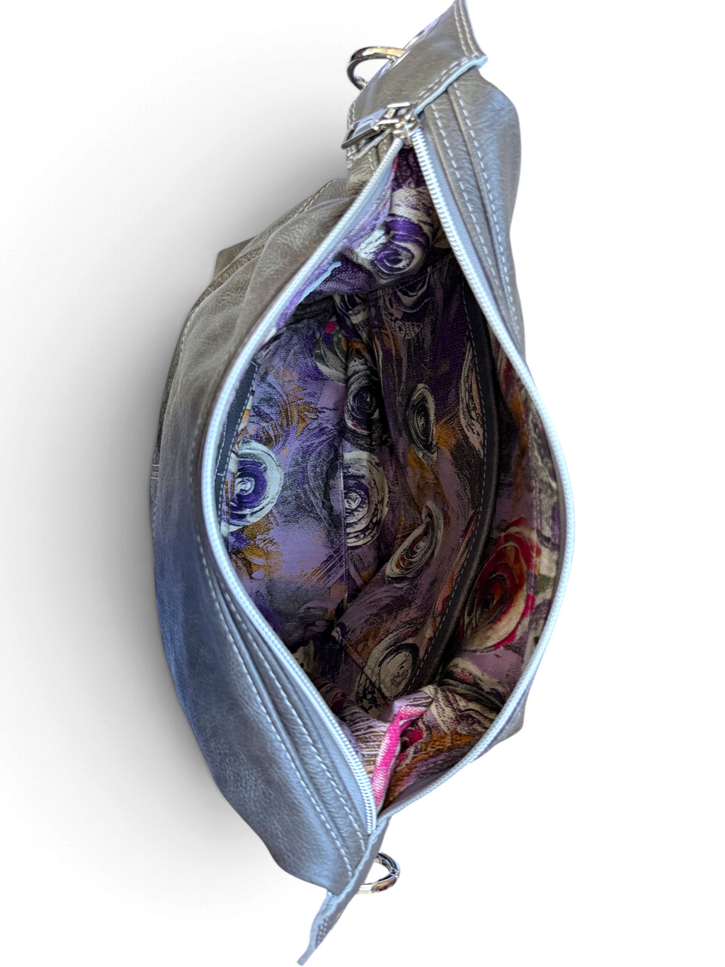 A dark grey leather shoulder bag shown open from a top-down view, revealing a highly detailed, colourful patterned fabric lining on the inside of the bag.
