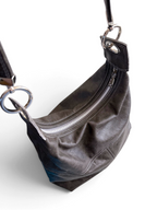 A dark grey leather shoulder bag with a slouchy crescent shaped top, featuring a silver-tone metal zipper, silver hardware, and a matching leather strap on a white background.