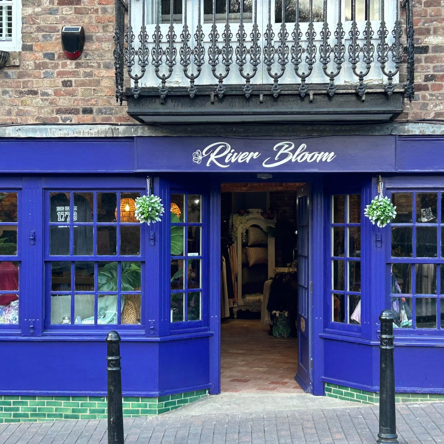 Blue store front with decorative metal railing above on a brick building.