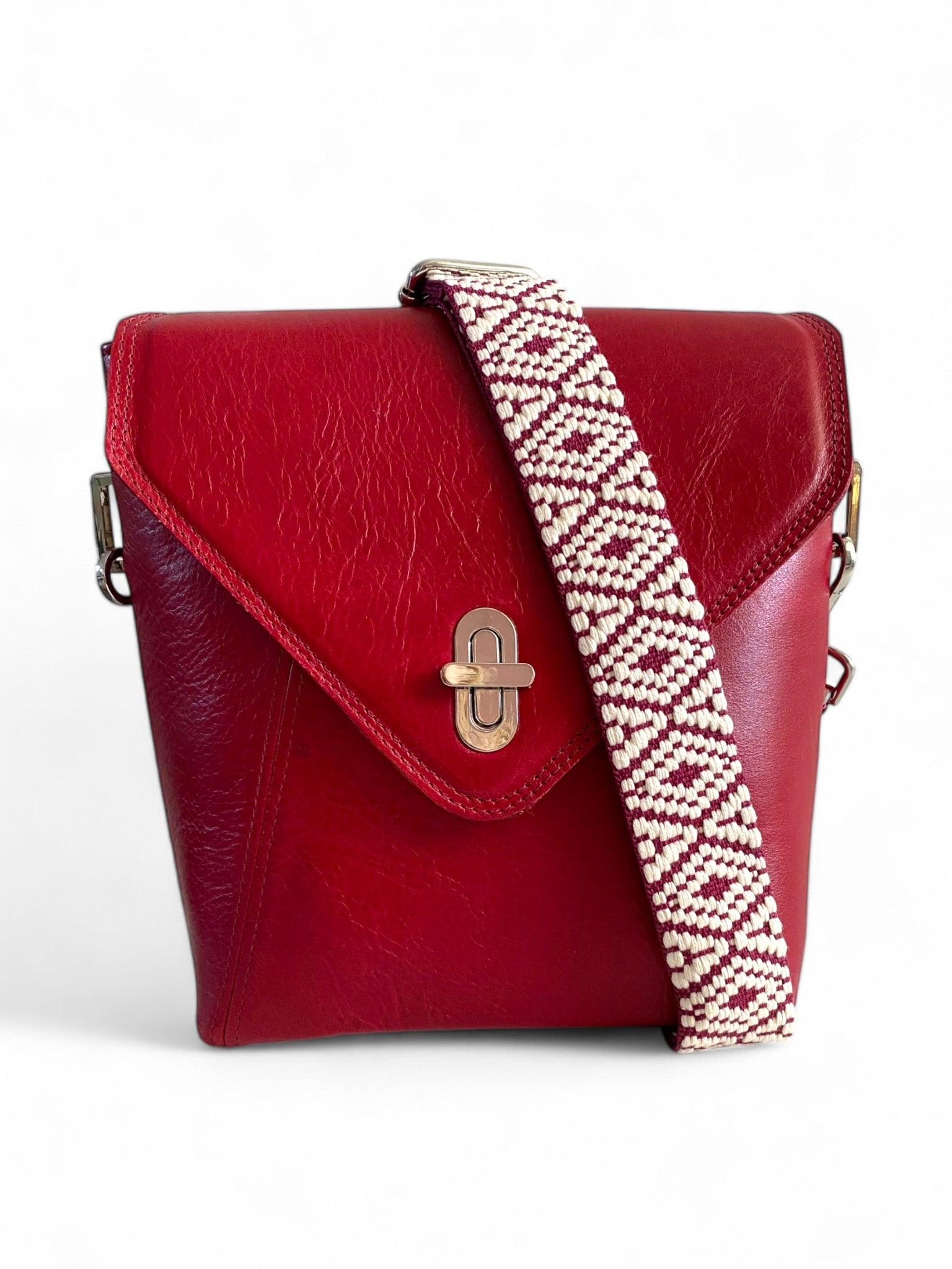A red leather, envelope shaped crossbody bag with a patterned woven strap and a silver twist-lock closure.