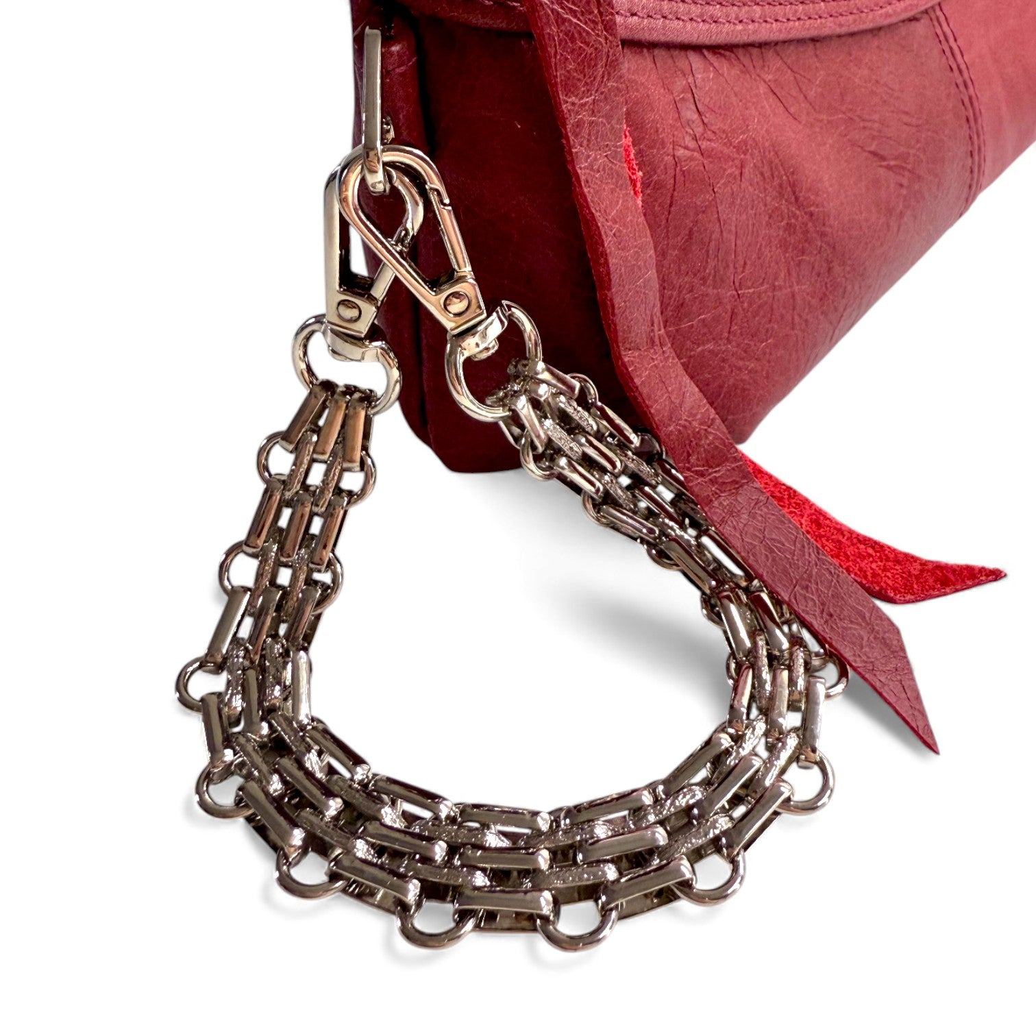 Multi link, silver metal chain, wrist strap accessory attached to a red leather bag