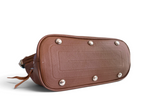 The underside of a brown leather bag, showing a rounded rectangular shaped base, with decorative silver-tone metal studs and a strap attachment, photographed on a white background.