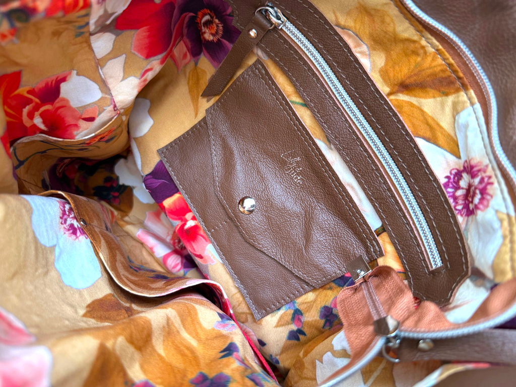 Close-up of a brown leather trimmed zippered pocket and a matching leather integrated purse pocket, withcard holder with a snap button. The lining is a colourful floral fabric interior.