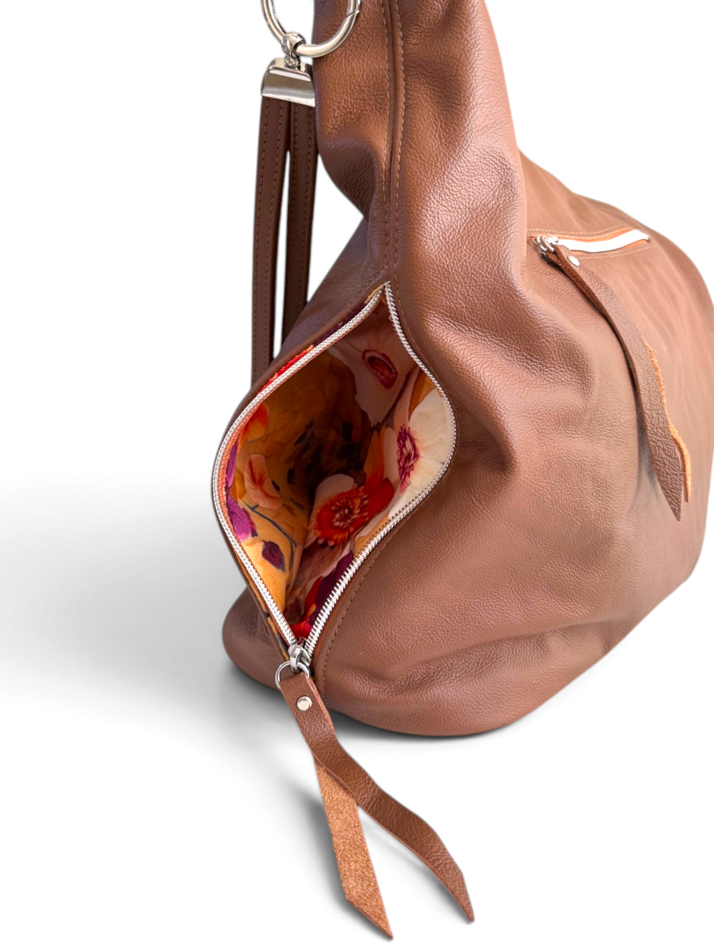 A close-up of a brown leather handbag with an open zipper revealing a colourful floral-patterned interior lining of a side pocket, set against a clean white background.